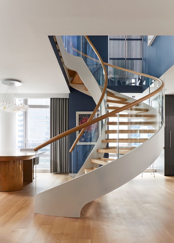 Aménagement d'un très grand escalier sans contremarche courbe contemporain avec des marches en bois et un garde-corps en verre.