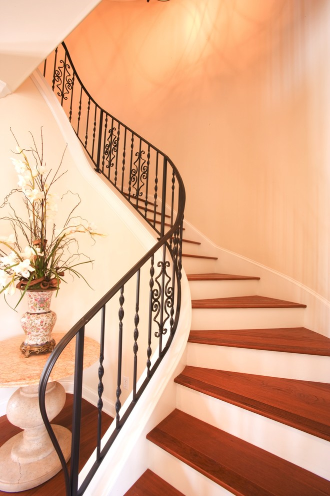На фото: большая изогнутая деревянная лестница в классическом стиле с деревянными ступенями и металлическими перилами с