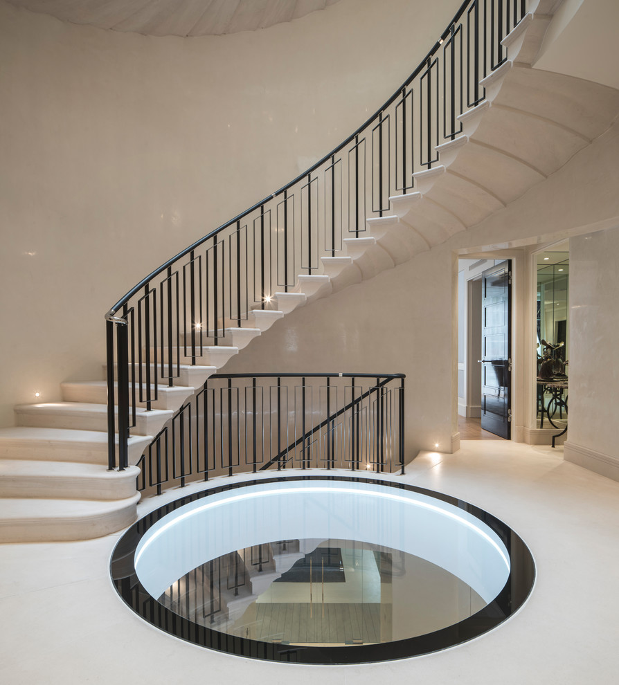 На фото: большая изогнутая лестница в стиле модернизм с ступенями из известняка, подступенками из известняка и металлическими перилами
