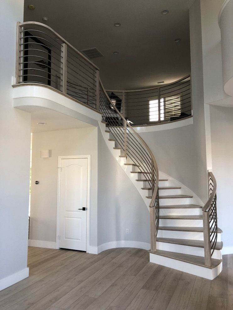 Стильный дизайн: большая изогнутая лестница в современном стиле с деревянными ступенями, крашенными деревянными подступенками и перилами из смешанных материалов - последний тренд