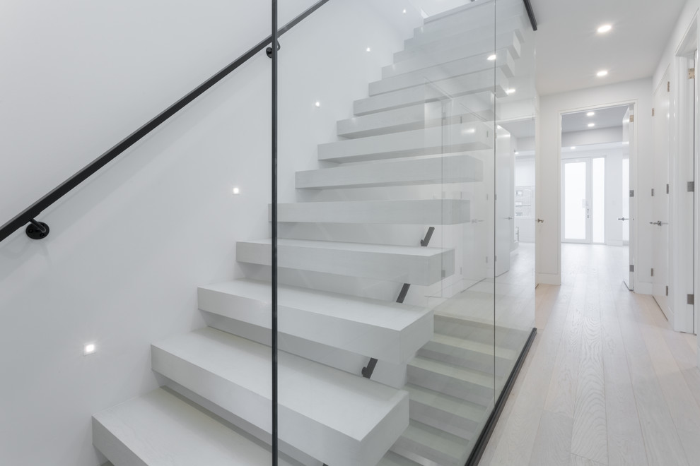 Cette image montre un grand escalier sans contremarche droit minimaliste avec un garde-corps en verre.