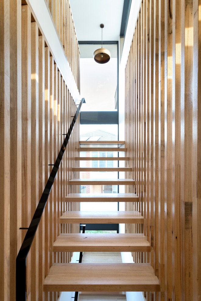 Cette image montre un grand escalier sans contremarche flottant design en bois avec des marches en bois et un garde-corps en métal.