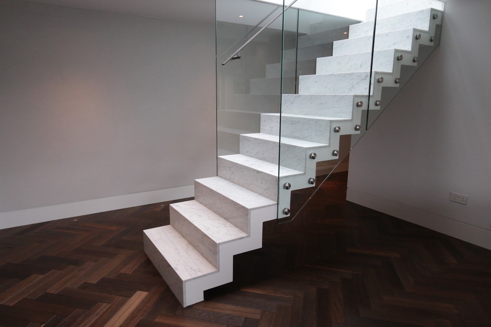 Photo of a contemporary straight glass railing staircase in London with marble treads and marble risers.