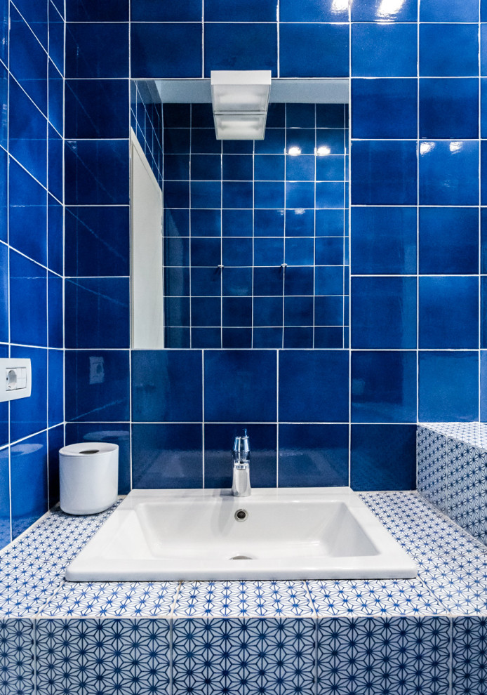 Inspiration för stora moderna blått en-suite badrum, med släta luckor, vita skåp, ett platsbyggt badkar, en toalettstol med separat cisternkåpa, blå kakel, keramikplattor, vita väggar, klinkergolv i keramik, ett nedsänkt handfat, kaklad bänkskiva och rött golv