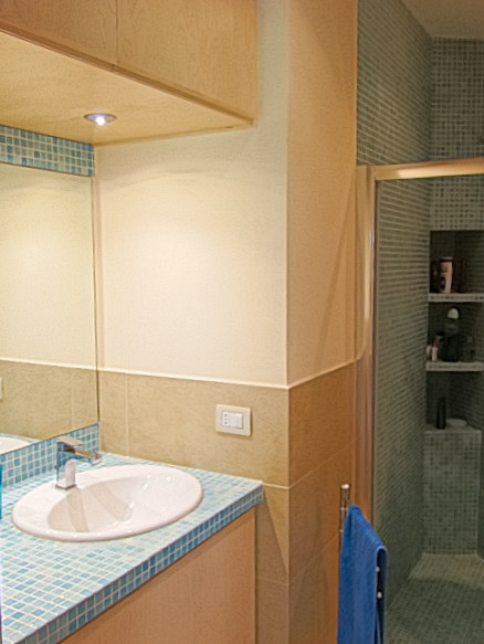 Immagine di una stanza da bagno con doccia moderna di medie dimensioni con ante lisce, ante in legno chiaro, doccia a filo pavimento, WC sospeso, piastrelle blu, piastrelle a mosaico, pareti bianche, pavimento in gres porcellanato, lavabo da incasso e top piastrellato