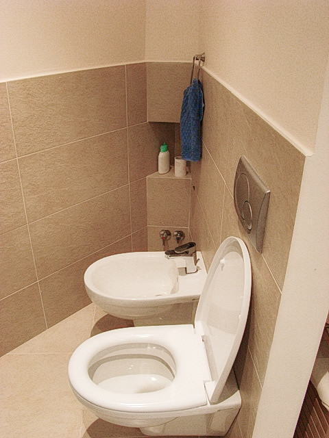 Idéer för att renovera ett mellanstort funkis badrum med dusch, med släta luckor, skåp i ljust trä, en kantlös dusch, en vägghängd toalettstol, blå kakel, mosaik, vita väggar, klinkergolv i porslin, ett nedsänkt handfat och kaklad bänkskiva