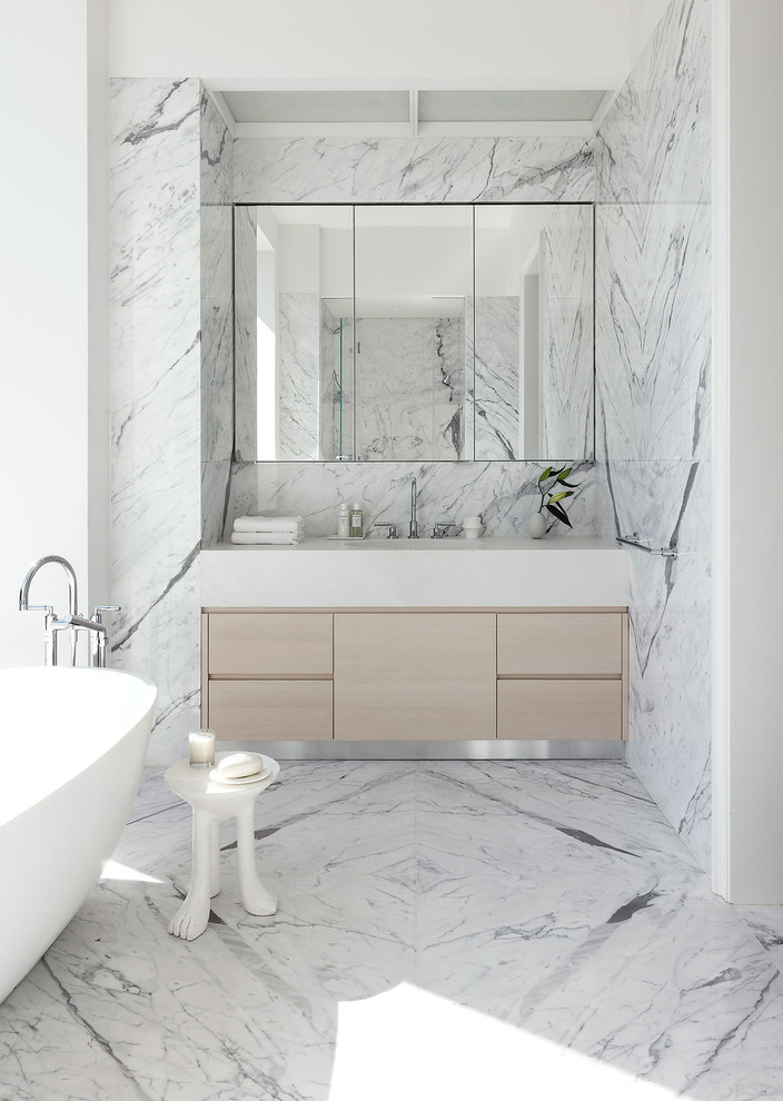 Idee per una stanza da bagno padronale design con ante lisce, ante in legno chiaro, vasca freestanding, piastrelle bianche, piastrelle in pietra, pareti bianche e pavimento in marmo