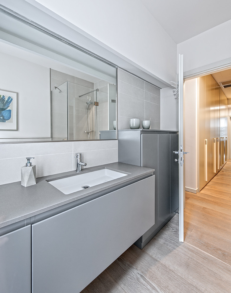 Стильный дизайн: ванная комната среднего размера в современном стиле с плоскими фасадами, серыми фасадами, серой плиткой, белыми стенами, светлым паркетным полом, врезной раковиной и бежевым полом - последний тренд