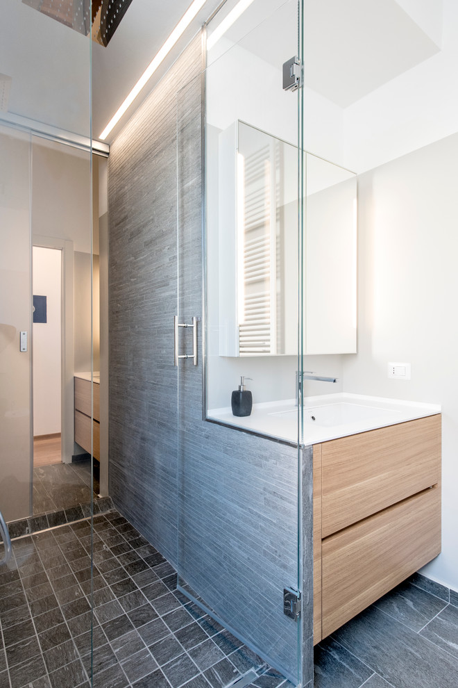 Design ideas for a medium sized contemporary shower room bathroom in Milan with flat-panel cabinets, light wood cabinets, a double shower, a wall mounted toilet, grey tiles, porcelain tiles, grey walls, porcelain flooring, a submerged sink and solid surface worktops.