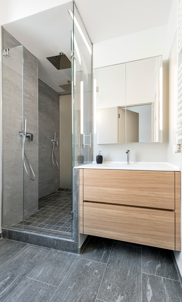 Inredning av ett modernt mellanstort badrum med dusch, med släta luckor, skåp i ljust trä, en dubbeldusch, grå kakel, porslinskakel, klinkergolv i porslin, grå väggar, ett undermonterad handfat, bänkskiva i akrylsten och dusch med gångjärnsdörr
