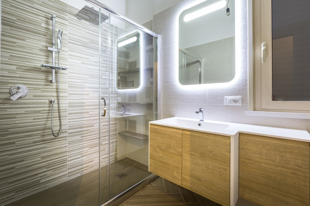 На фото: ванная комната в современном стиле с плоскими фасадами, душем без бортиков, душевой кабиной, душем с раздвижными дверями, белой столешницей, светлыми деревянными фасадами, разноцветной плиткой, удлиненной плиткой, белыми стенами и монолитной раковиной с