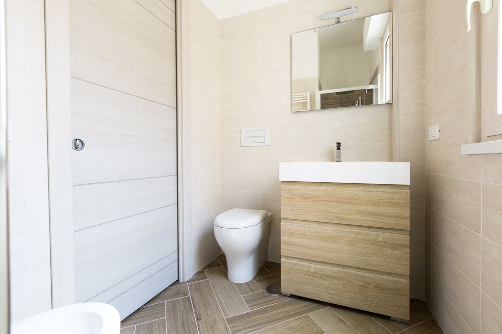 Modelo de cuarto de baño actual pequeño con puertas de armario de madera clara, sanitario de pared, baldosas y/o azulejos beige, paredes beige, suelo beige y armarios con paneles lisos