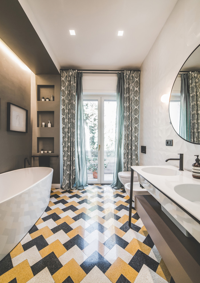 フィレンツェにあるコンテンポラリースタイルのおしゃれな浴室 (フラットパネル扉のキャビネット、グレーのキャビネット、置き型浴槽、グレーの壁、一体型シンク、マルチカラーの床、白い洗面カウンター、洗面台2つ) の写真