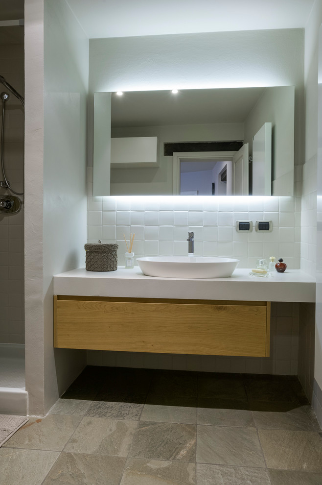 На фото: ванная комната среднего размера, в белых тонах с отделкой деревом в современном стиле с светлыми деревянными фасадами, раздельным унитазом, белой плиткой, керамической плиткой, белыми стенами, полом из сланца, настольной раковиной, столешницей из искусственного камня, серым полом, шторкой для ванной, стеклянными фасадами, душем в нише, душевой кабиной, белой столешницей, нишей, тумбой под одну раковину и встроенной тумбой с