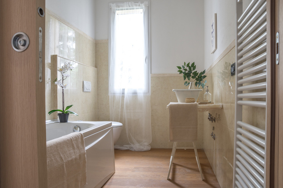 Cette photo montre une salle de bain chic avec une vasque, un carrelage beige, un mur blanc, un sol en bois brun et une baignoire indépendante.
