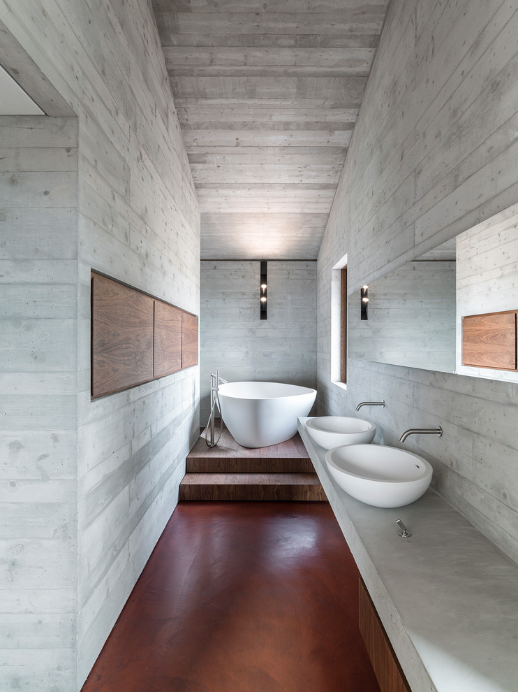 Пример оригинального дизайна: большая главная ванная комната в стиле модернизм с фасадами цвета дерева среднего тона, бетонным полом, настольной раковиной, столешницей из бетона, красным полом, отдельно стоящей ванной, душем над ванной, серыми стенами и открытым душем