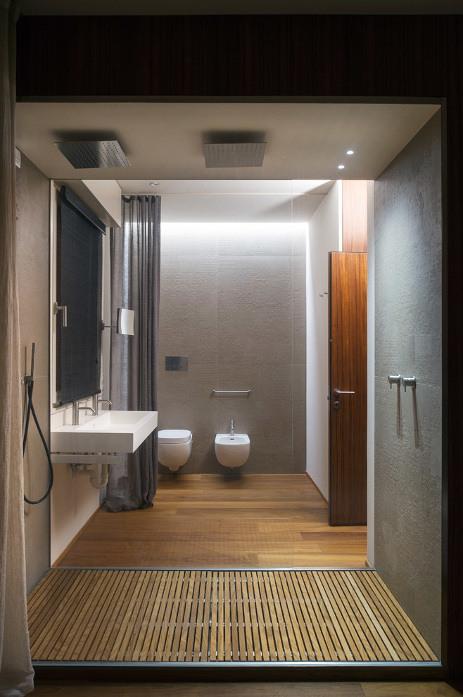 Cette image montre une salle de bain design avec un lavabo suspendu, un bidet et un sol en bois brun.