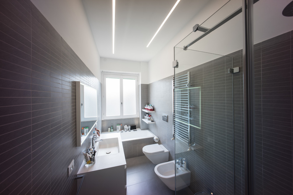 Свежая идея для дизайна: главная ванная комната среднего размера в современном стиле с плоскими фасадами, белыми фасадами, полновстраиваемой ванной, угловым душем, инсталляцией, серой плиткой, керамогранитной плиткой, серыми стенами, полом из керамогранита, монолитной раковиной, столешницей из искусственного кварца, серым полом и душем с распашными дверями - отличное фото интерьера