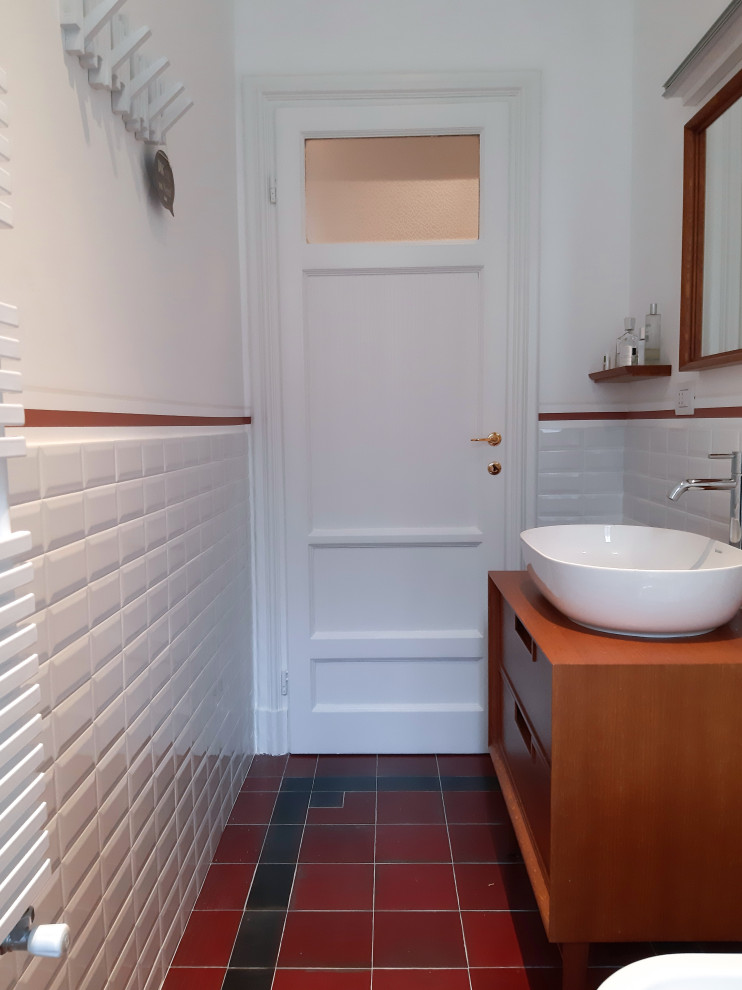 Inredning av ett 50 tals mellanstort brun brunt badrum med dusch, med luckor med infälld panel, skåp i mörkt trä, en dusch i en alkov, en toalettstol med separat cisternkåpa, vit kakel, porslinskakel, vita väggar, klinkergolv i keramik, ett fristående handfat, träbänkskiva, rött golv och dusch med skjutdörr