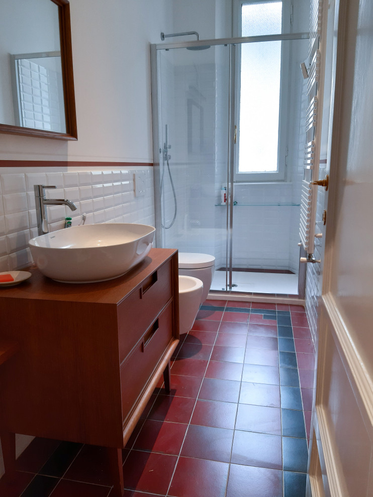 Пример оригинального дизайна: ванная комната среднего размера в стиле ретро с фасадами с утопленной филенкой, темными деревянными фасадами, душем в нише, раздельным унитазом, белой плиткой, керамогранитной плиткой, белыми стенами, полом из керамической плитки, душевой кабиной, настольной раковиной, столешницей из дерева, красным полом, душем с раздвижными дверями, коричневой столешницей, тумбой под одну раковину и напольной тумбой