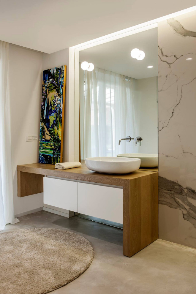 На фото: ванная комната в современном стиле с плоскими фасадами, белыми фасадами, белой плиткой, плиткой из листового камня, серыми стенами, бетонным полом, настольной раковиной, столешницей из дерева, серым полом и коричневой столешницей