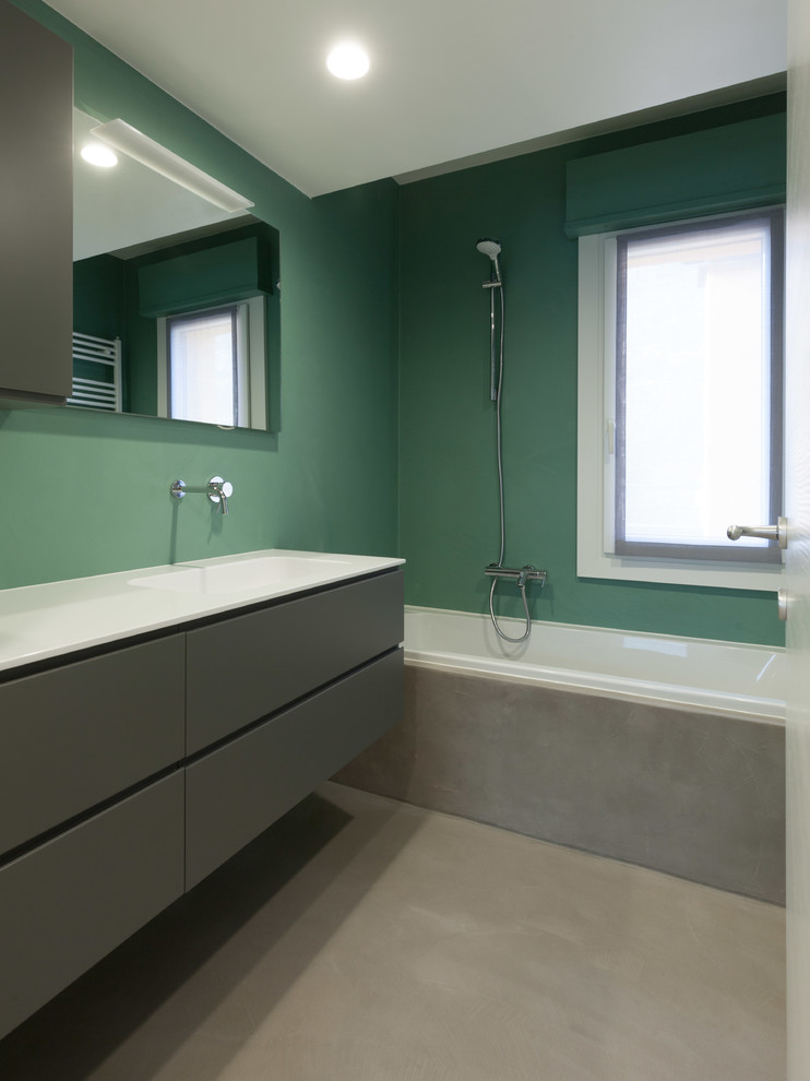Inredning av ett modernt litet en-suite badrum, med släta luckor, grå skåp, ett platsbyggt badkar, en vägghängd toalettstol, gröna väggar, betonggolv, ett integrerad handfat, bänkskiva i kvarts och grått golv