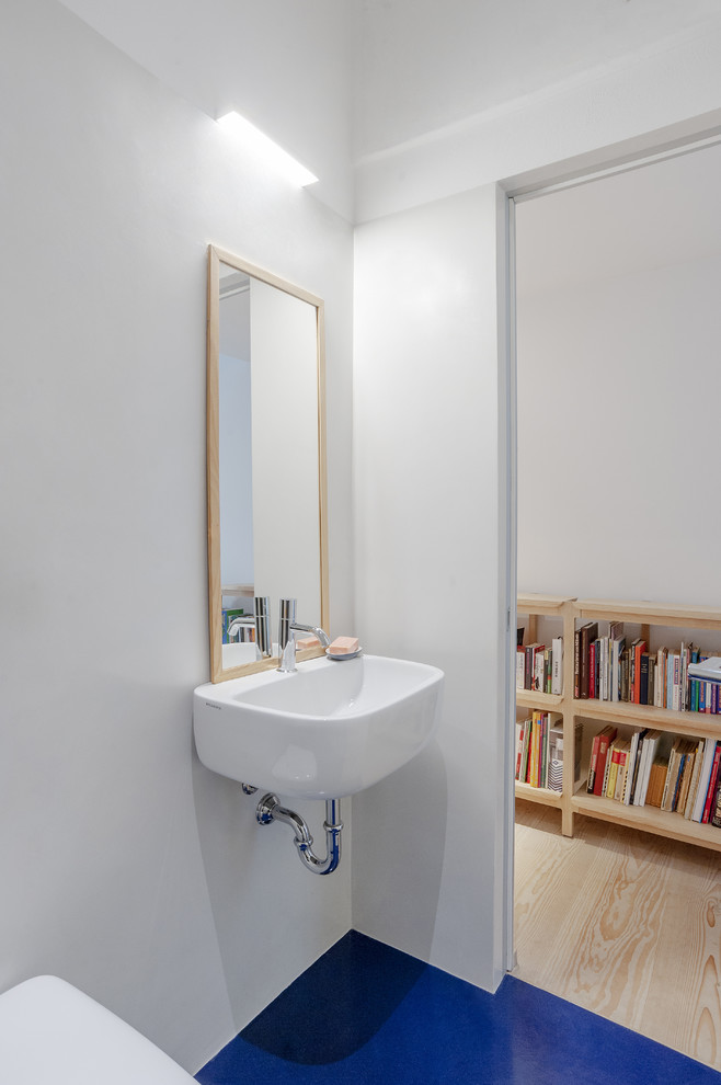 Bild på ett skandinaviskt badrum, med en vägghängd toalettstol, vita väggar, ett väggmonterat handfat och blått golv