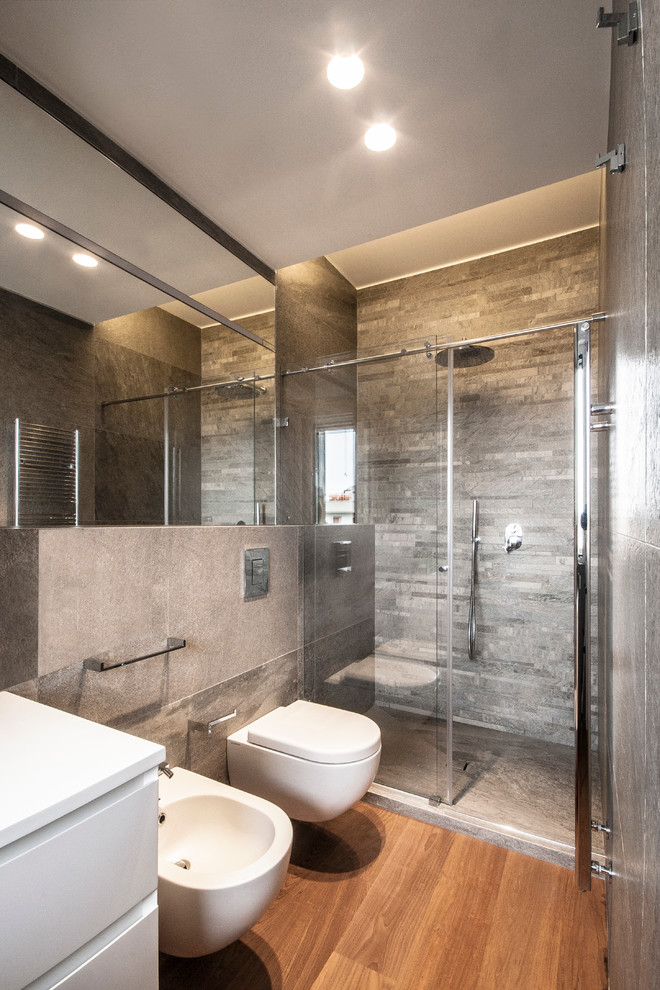 Modern inredning av ett badrum, med en vägghängd toalettstol, en dusch i en alkov, mellanmörkt trägolv och grå kakel