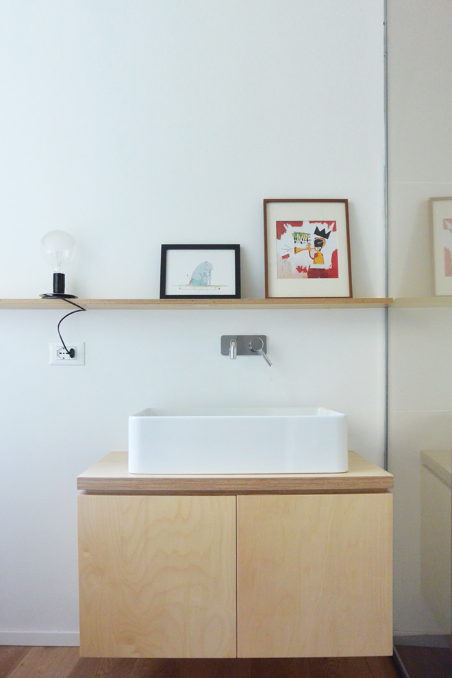 Nordisk inredning av ett litet badrum med dusch, med släta luckor, skåp i ljust trä, en kantlös dusch, en vägghängd toalettstol, beige kakel, keramikplattor, vita väggar, ljust trägolv, ett fristående handfat, träbänkskiva och dusch med gångjärnsdörr