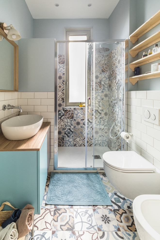 На фото: ванная комната в скандинавском стиле с плоскими фасадами, синими фасадами, душем в нише, инсталляцией, белой плиткой, плиткой кабанчик, синими стенами, душевой кабиной, настольной раковиной, столешницей из дерева, разноцветным полом, душем с раздвижными дверями и коричневой столешницей с