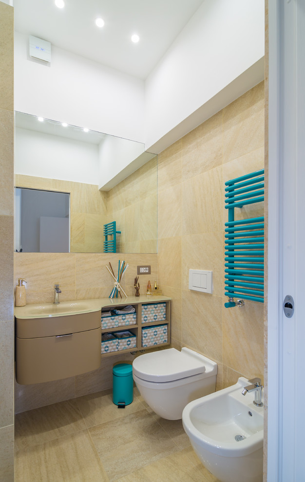 Modelo de cuarto de baño actual con lavabo integrado, armarios con paneles lisos, encimera de vidrio, sanitario de pared, baldosas y/o azulejos beige y puertas de armario beige