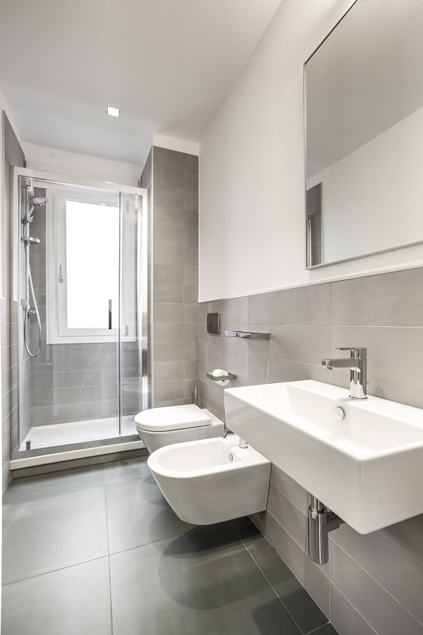 Cette image montre une petite salle de bain design avec WC suspendus, un carrelage gris, des carreaux de porcelaine, un mur blanc, un sol en carrelage de porcelaine, un lavabo suspendu, un sol vert et une cabine de douche à porte battante.