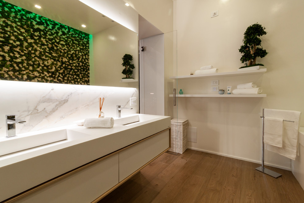 Inspiration pour une salle de bain design avec un placard à porte plane, des portes de placard blanches, un carrelage blanc, un mur blanc, un sol en bois brun, un lavabo intégré, un sol marron et un plan de toilette blanc.