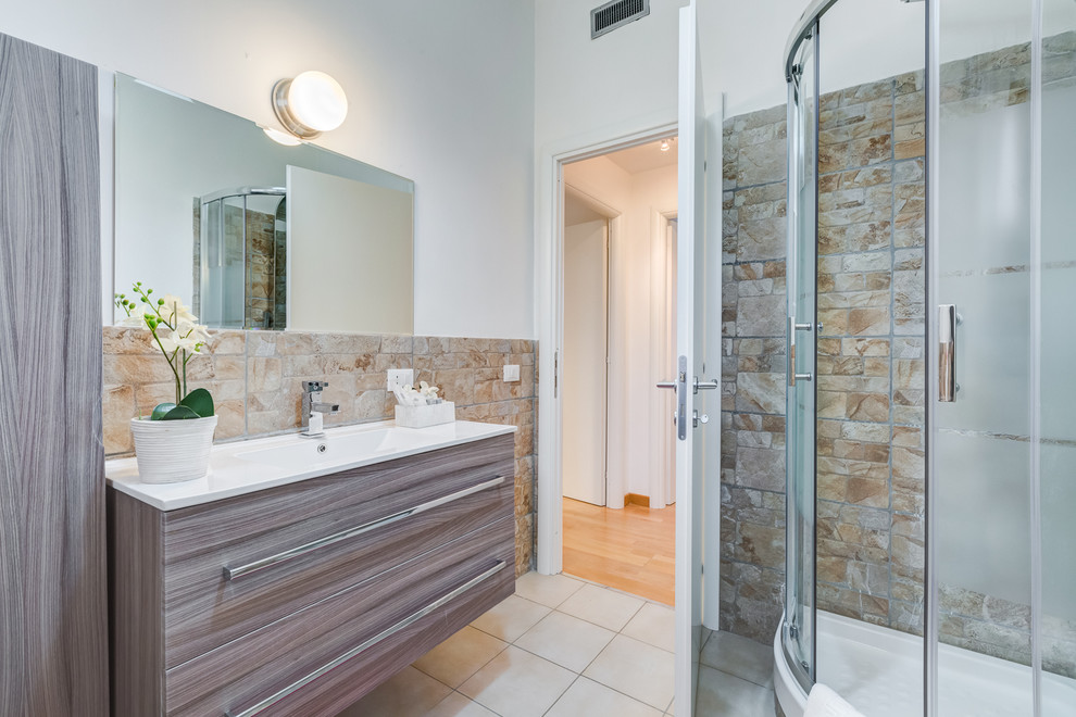 На фото: ванная комната в современном стиле с плоскими фасадами, фасадами цвета дерева среднего тона, угловым душем, каменной плиткой, белыми стенами и монолитной раковиной с