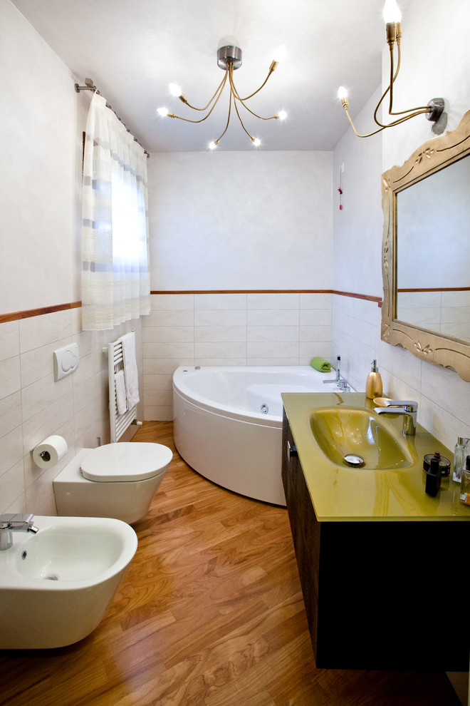 Idéer för eklektiska en-suite badrum, med ett integrerad handfat, bänkskiva i glas, ett hörnbadkar, vit kakel, vita väggar, mellanmörkt trägolv, släta luckor och svarta skåp