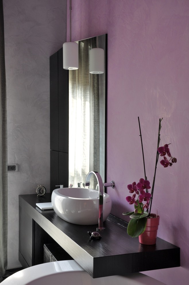 Réalisation d'une salle de bain principale design avec des portes de placard noires, une baignoire indépendante, WC suspendus, un mur violet, un sol en carrelage de céramique, une vasque, un plan de toilette en bois, un sol noir et un plan de toilette noir.