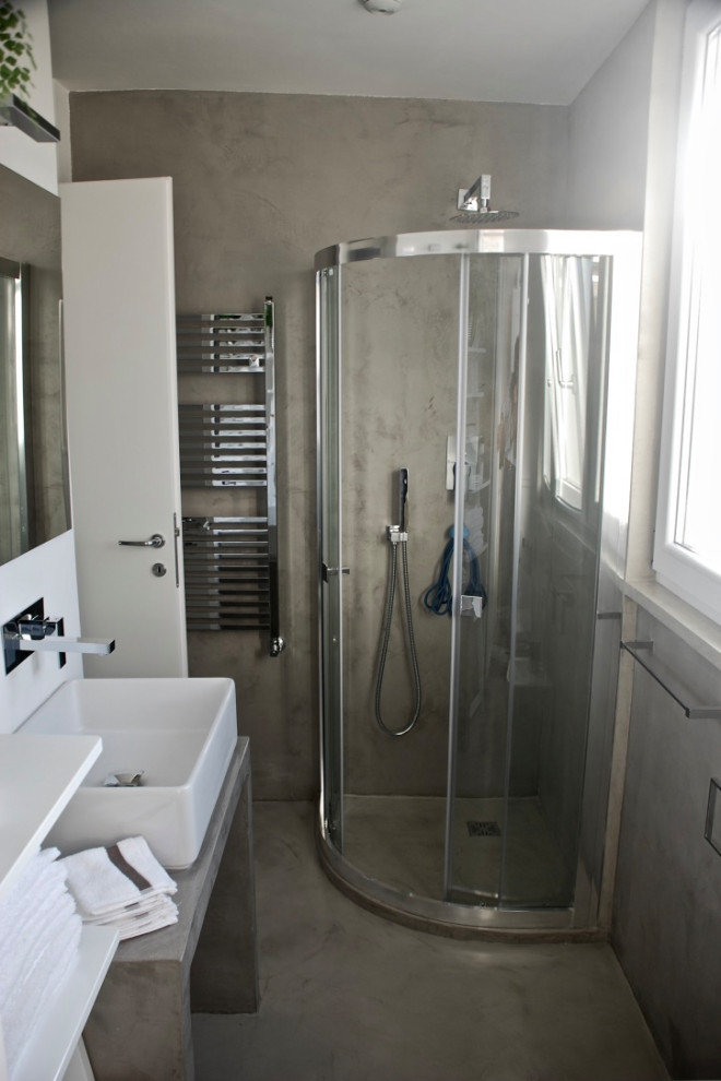 Foto på ett mellanstort nordiskt grå badrum med dusch, med öppna hyllor, grå skåp, en hörndusch, en toalettstol med separat cisternkåpa, grå väggar, betonggolv, ett fristående handfat, bänkskiva i betong, grått golv och dusch med skjutdörr