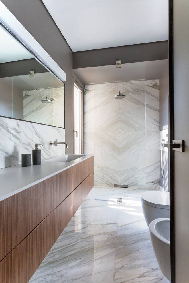 Immagine di una stanza da bagno con doccia design con ante in legno bruno, doccia a filo pavimento, piastrelle di marmo, top bianco, ante lisce, bidè, pareti grigie, lavabo integrato, pavimento grigio e porta doccia a battente