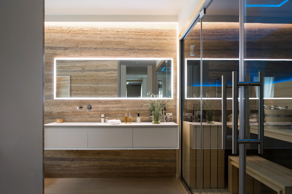 Cette photo montre une salle de bain principale tendance avec un placard à porte plane, des portes de placard blanches, un carrelage de pierre, un mur beige, un sol en bois brun et un lavabo intégré.