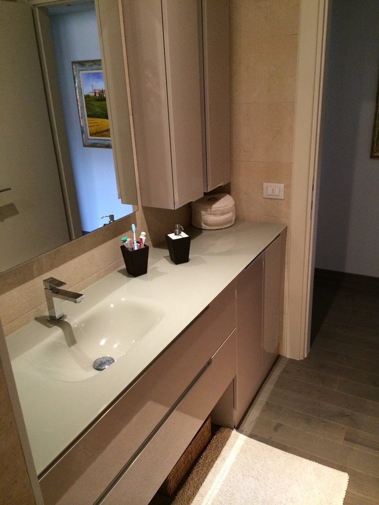 Inredning av ett modernt litet badrum med dusch, med släta luckor, beige skåp, en kantlös dusch, en vägghängd toalettstol, beige kakel, porslinskakel, beige väggar, målat trägolv, ett integrerad handfat och bänkskiva i glas