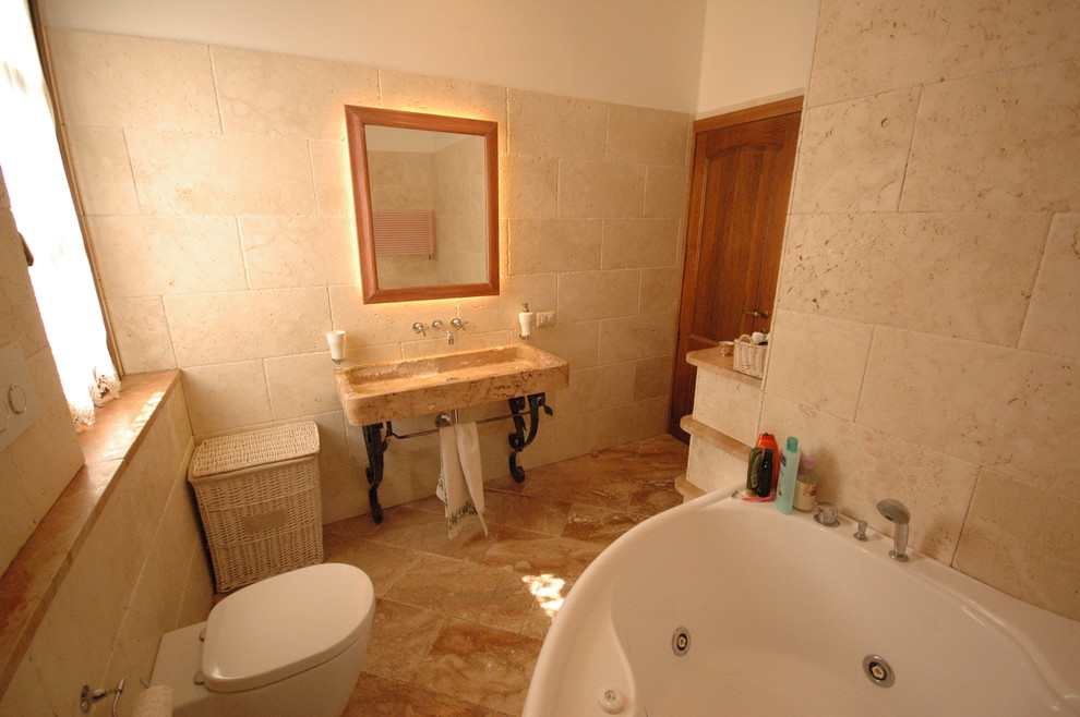 На фото: ванная комната среднего размера в современном стиле с открытыми фасадами, бежевыми фасадами, гидромассажной ванной, душевой комнатой, раздельным унитазом, бежевой плиткой, плиткой из травертина, бежевыми стенами, полом из травертина, душевой кабиной, настольной раковиной, столешницей из известняка, красным полом и открытым душем с
