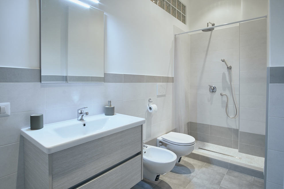 На фото: серо-белая ванная комната среднего размера в стиле модернизм с плоскими фасадами, светлыми деревянными фасадами, душем в нише, инсталляцией, белой плиткой, серой плиткой, керамической плиткой, белыми стенами, полом из керамической плитки, душевой кабиной, монолитной раковиной и шторкой для ванной с