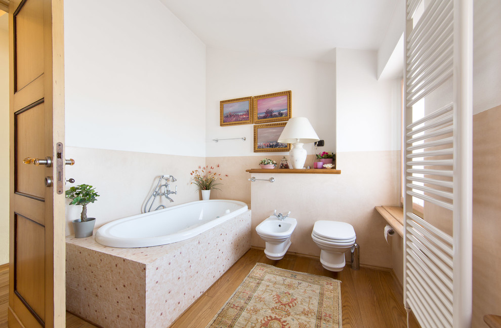 Klassisches Badezimmer mit Einbaubadewanne, Toilette mit Aufsatzspülkasten, rosa Wandfarbe und hellem Holzboden in Sonstige