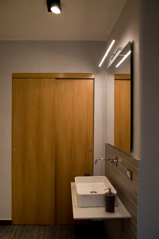 Пример оригинального дизайна: ванная комната среднего размера в современном стиле с плоскими фасадами, светлыми деревянными фасадами, душем без бортиков, инсталляцией, серой плиткой, керамогранитной плиткой, серыми стенами, полом из керамогранита, душевой кабиной, настольной раковиной, столешницей из кварцита, серым полом, открытым душем, белой столешницей, нишей, тумбой под одну раковину, подвесной тумбой и многоуровневым потолком