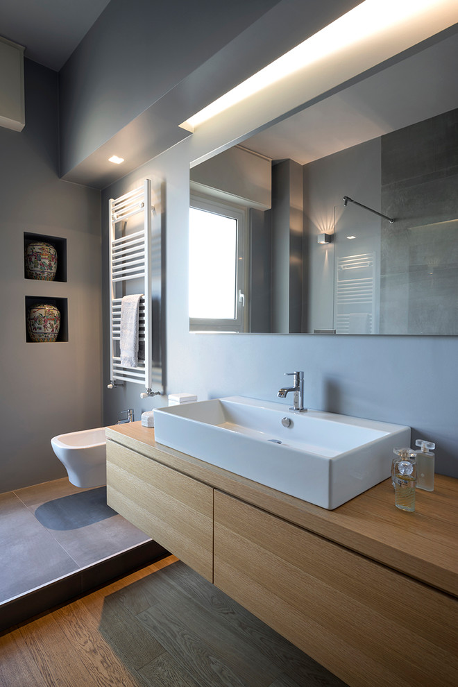 Idée de décoration pour une grande salle d'eau minimaliste en bois clair avec un placard à porte plane, une douche ouverte, WC suspendus, un mur gris, parquet clair, une vasque, un sol beige et un plan de toilette beige.