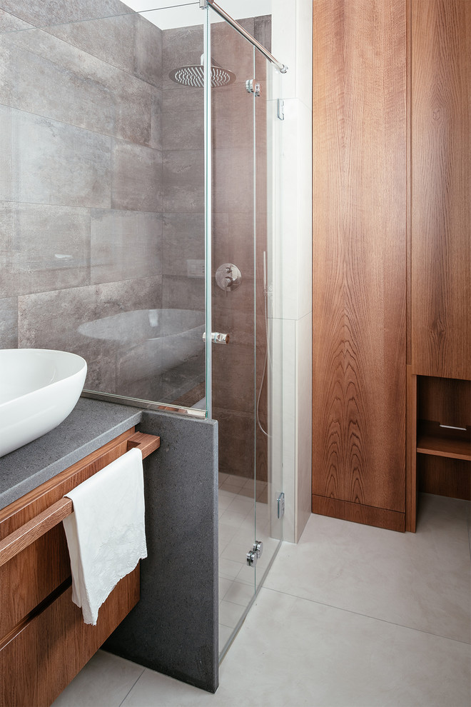 Design ideas for a contemporary shower room bathroom in Naples with flat-panel cabinets, medium wood cabinets, a built-in shower, a wall mounted toilet, grey tiles, porcelain tiles, beige walls, porcelain flooring, a vessel sink, marble worktops, beige floors, a hinged door and black worktops.