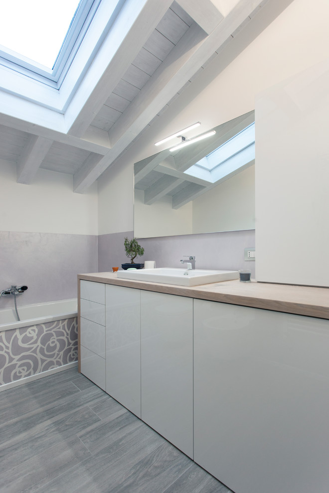 На фото: главная ванная комната среднего размера в стиле модернизм с плоскими фасадами, белыми фасадами, накладной ванной, серыми стенами, полом из керамогранита, раковиной с несколькими смесителями и столешницей из дерева с