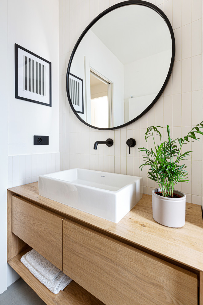 Пример оригинального дизайна: маленькая ванная комната в скандинавском стиле с плоскими фасадами, светлыми деревянными фасадами, душем без бортиков, инсталляцией, белой плиткой, удлиненной плиткой, белыми стенами, бетонным полом, душевой кабиной, настольной раковиной, столешницей из дерева, серым полом, открытым душем, тумбой под одну раковину, подвесной тумбой и многоуровневым потолком для на участке и в саду