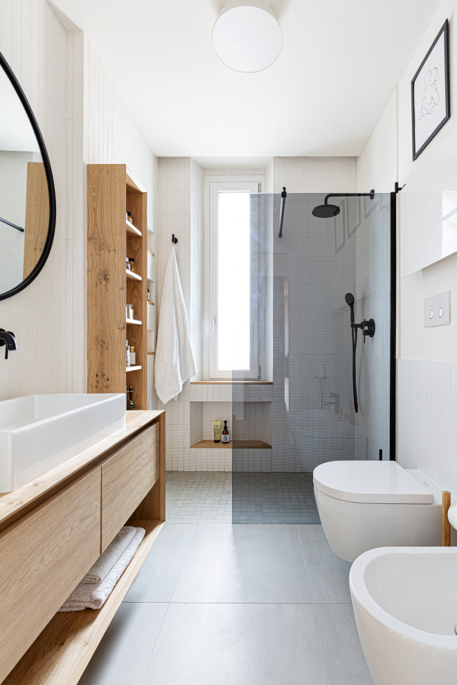 Exempel på ett litet skandinaviskt badrum med dusch, med släta luckor, skåp i ljust trä, en kantlös dusch, en vägghängd toalettstol, vit kakel, stickkakel, vita väggar, betonggolv, ett fristående handfat, träbänkskiva, grått golv och med dusch som är öppen