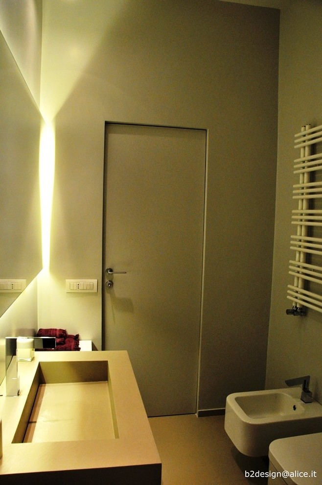 Modelo de cuarto de baño principal moderno de tamaño medio con puertas de armario blancas, bañera encastrada, sanitario de pared, paredes grises, suelo de baldosas de porcelana, lavabo tipo consola y encimera de laminado